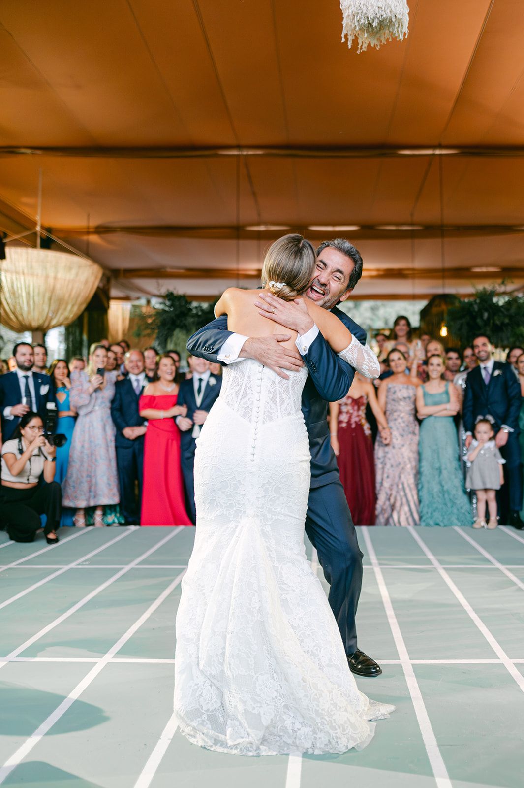 Bride and groom share an emotional first dance hug in a lace wedding gown at an elegant outdoor reception.