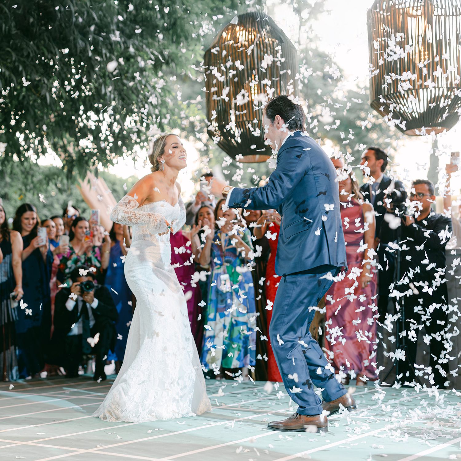 Bride and groom celebrate outdoor wedding exit with white confetti petals shower.