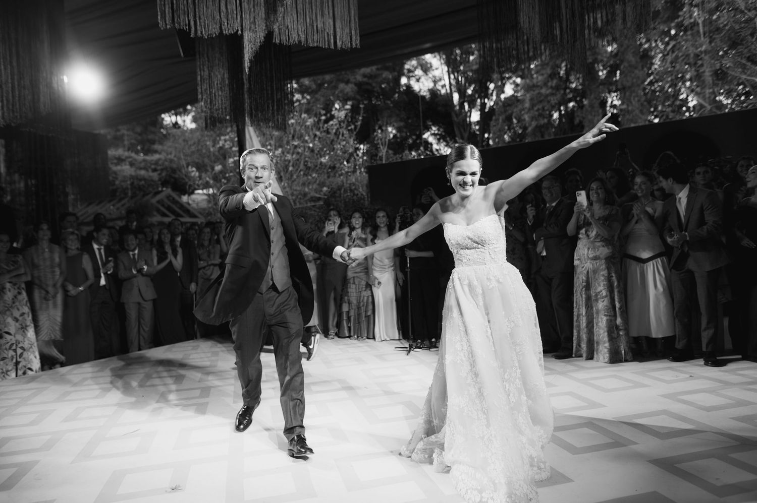 Couple dances joyfully on a white dance floor beneath elegant hanging fringe decor.