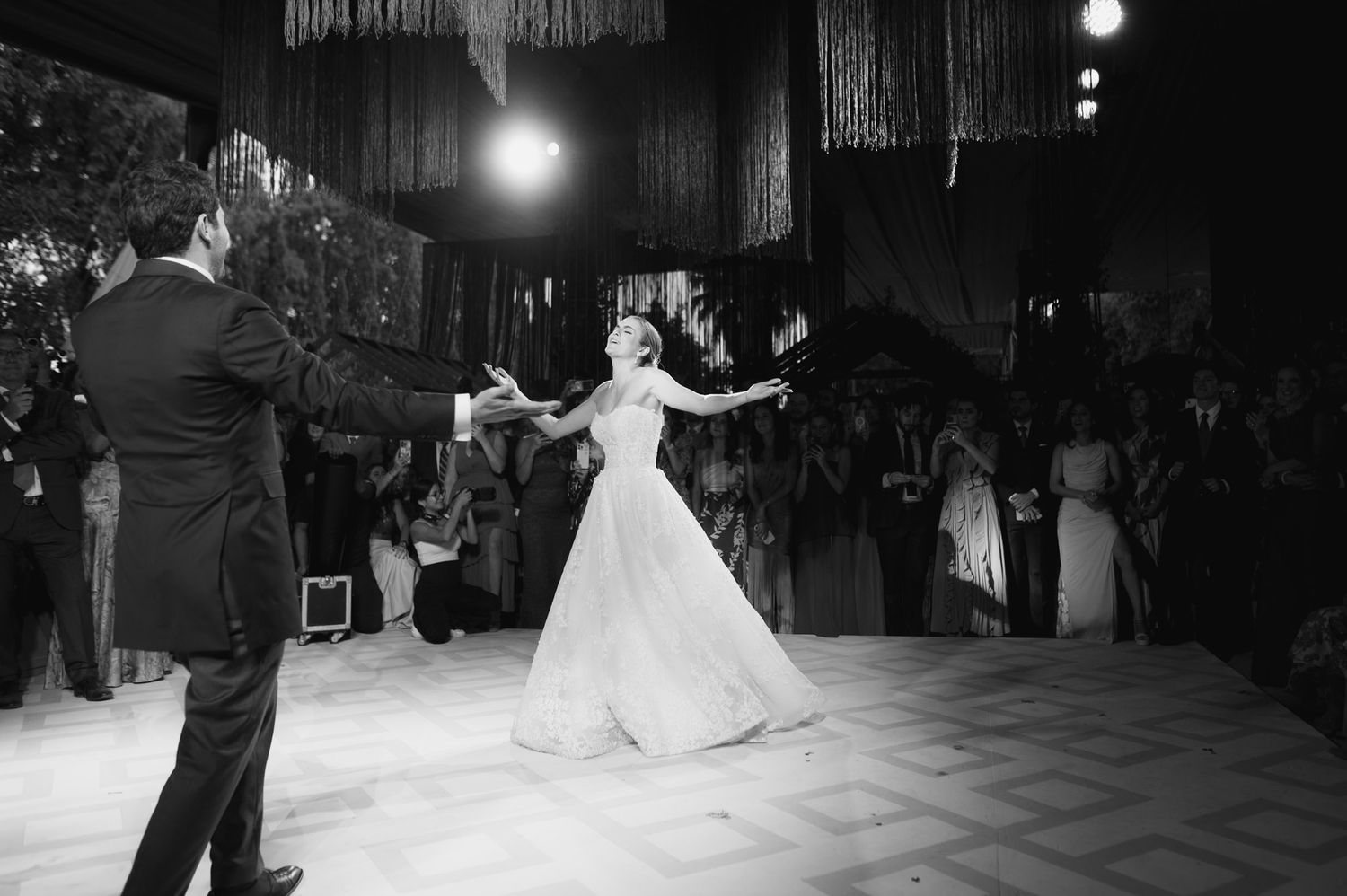 Black and white photo of couple dancing with dramatic lighting and fringe decor above.