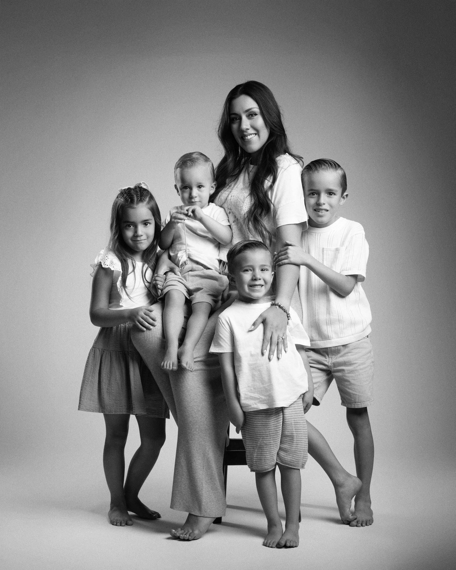 Black and white studio portrait of a mother smiling with her four young children posing together.