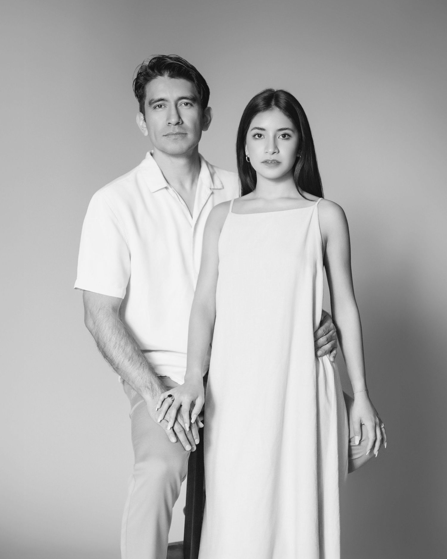 Black and white studio portrait of a man and woman in elegant white outfits.