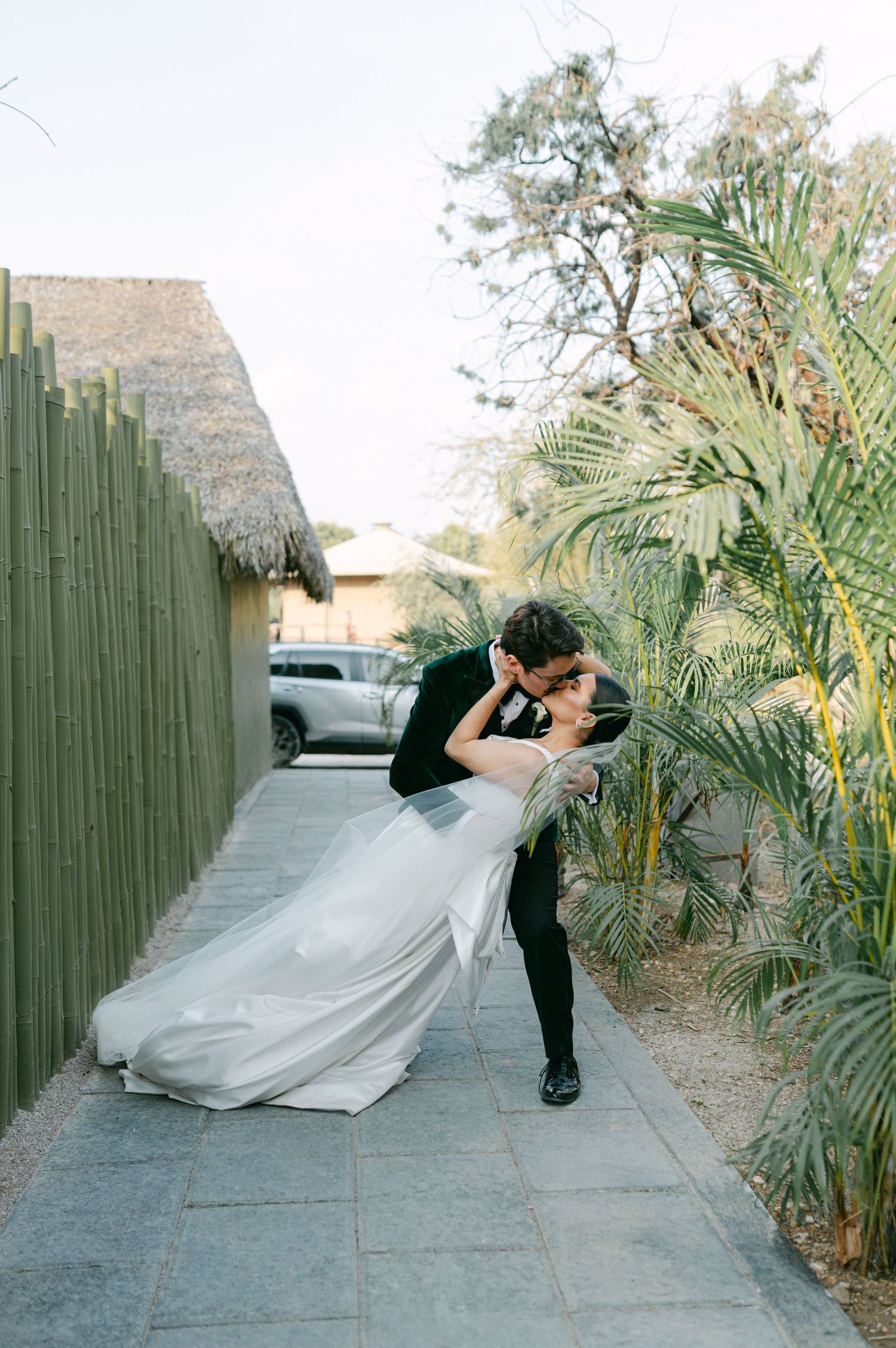 Bride and groom sharing a romantic dip kiss in a tropical garden pathway on their wedding day.