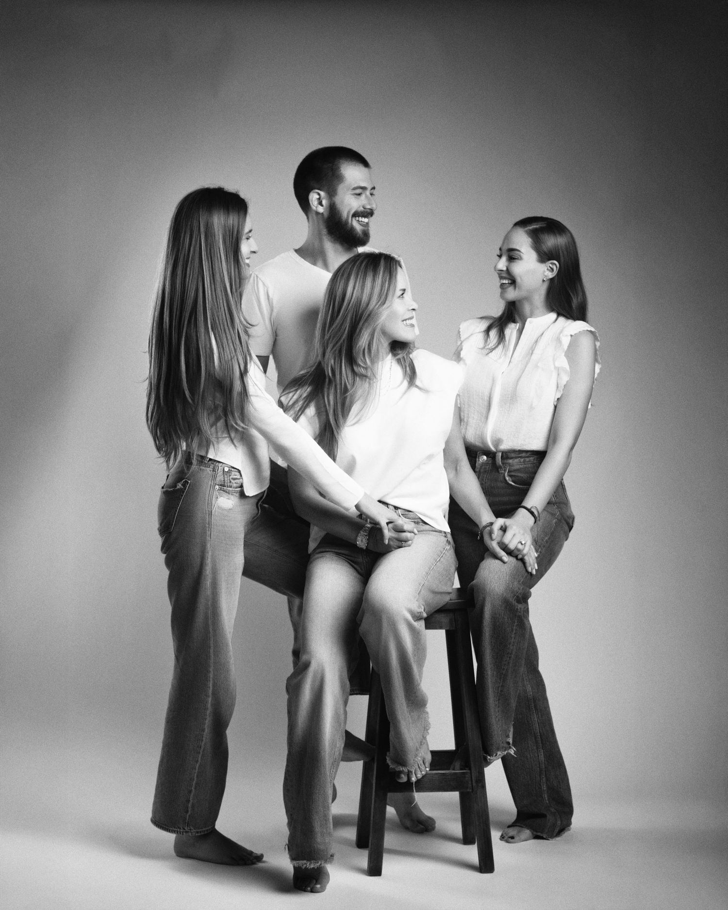 Black and white studio photo of a family of four laughing and interacting naturally around a wooden stool.