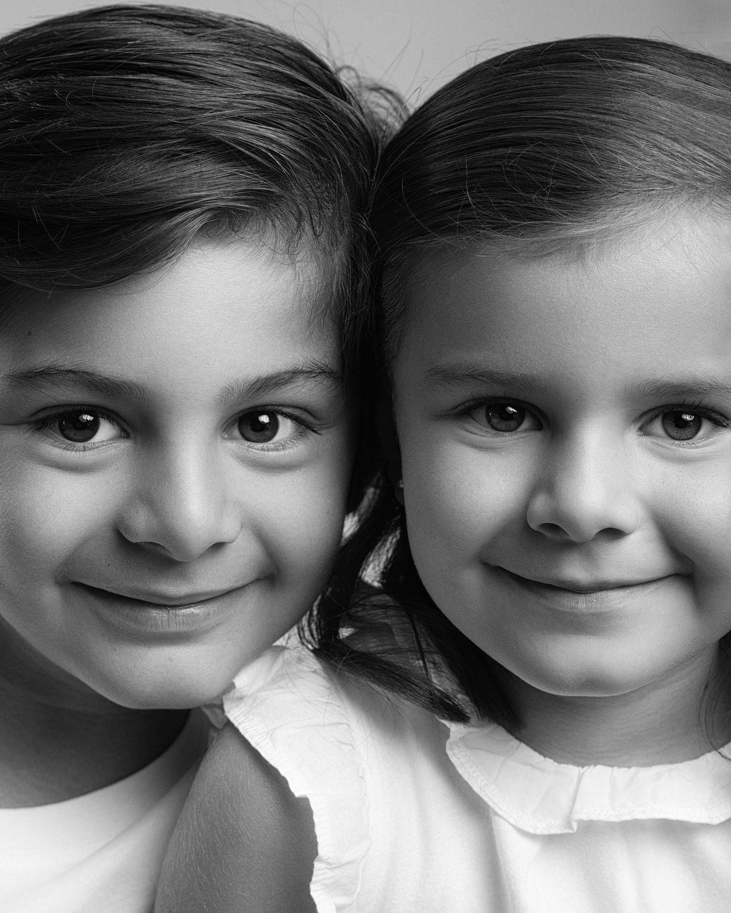 Black and white close-up portrait of two young sisters smiling at the camera.