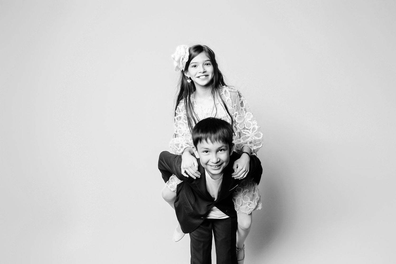 Black and white studio portrait of a girl riding piggyback on a smiling boy.