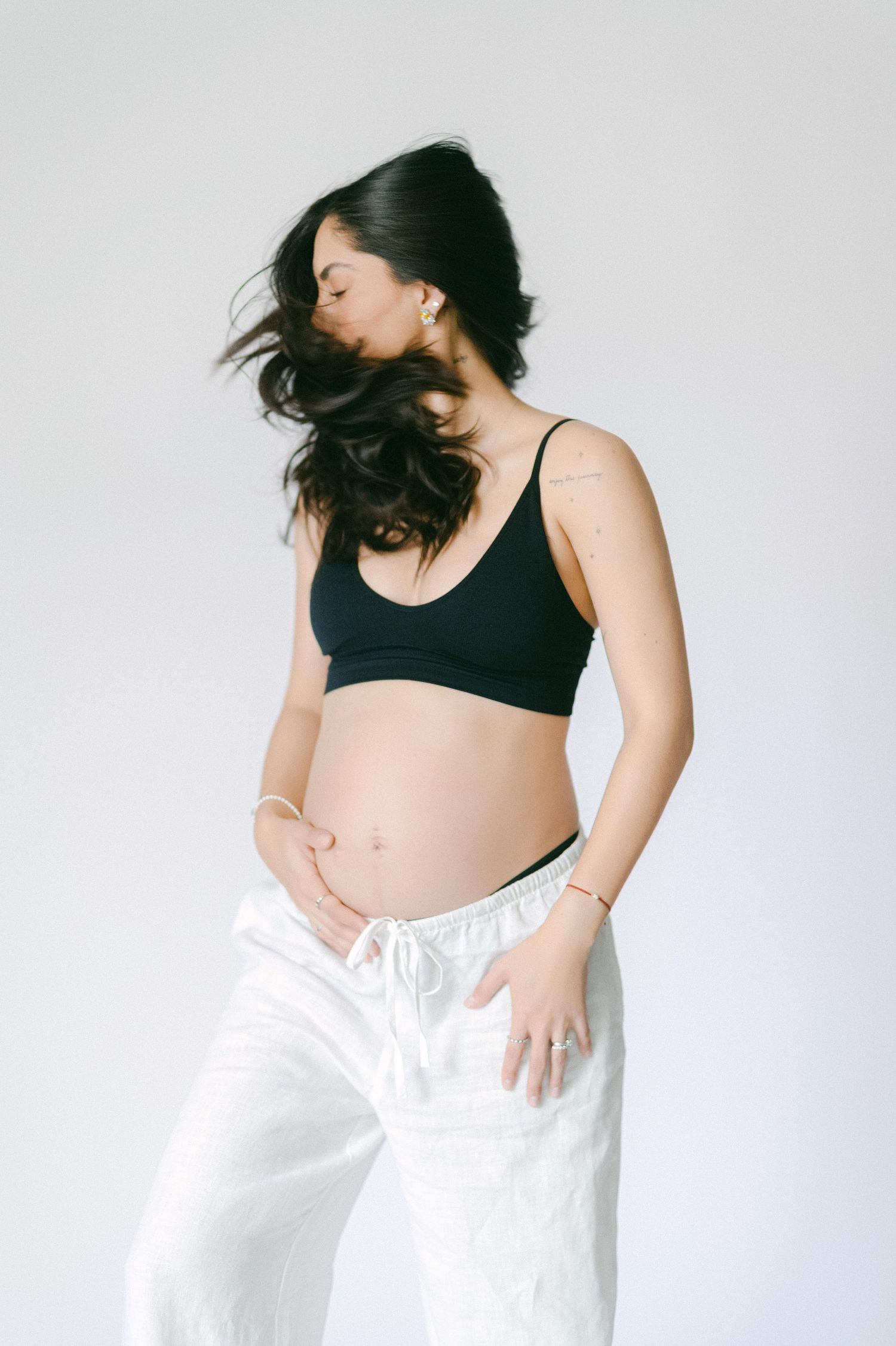 Pregnant woman in black crop top and white pants holding her baby bump.