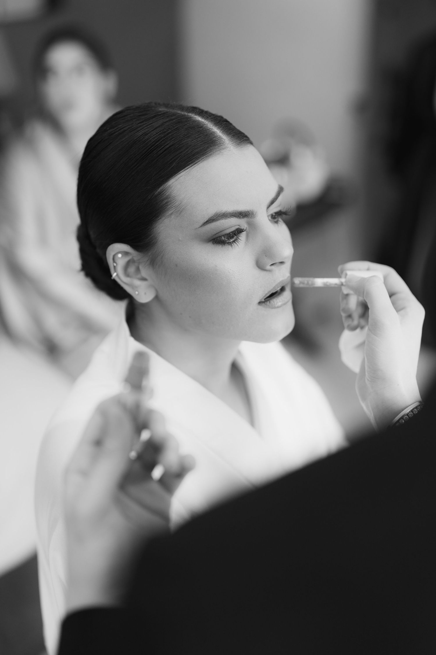 Black and white photo of a bride getting makeup applied before her wedding ceremony.
