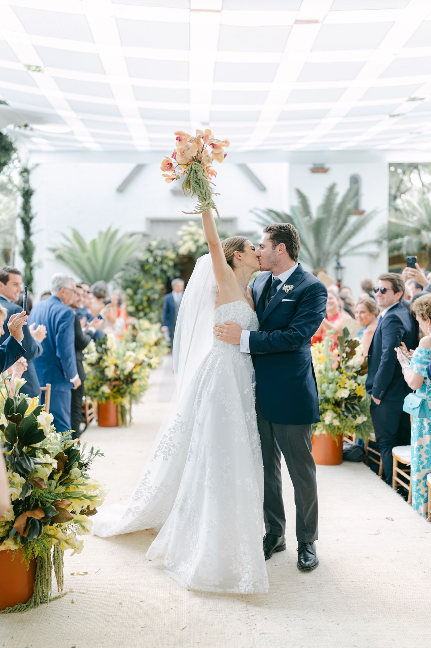 Bright indoor ceremony space decorated with tropical plants and elegant white ceiling details.