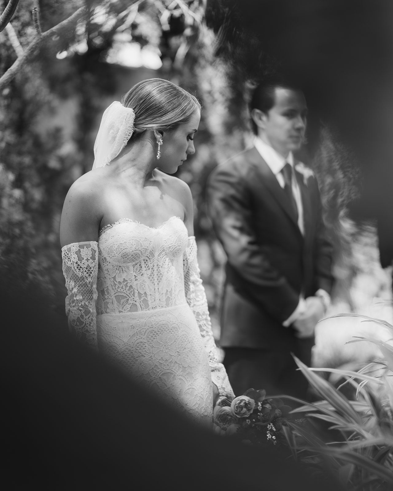 Black and white close-up of bride in off-shoulder lace gown during an outdoor garden ceremony.