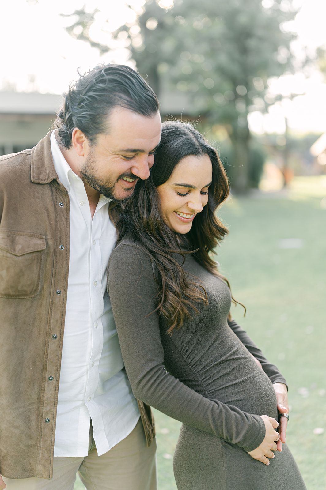Expecting couple embracing outdoors during maternity photo session in golden sunlight.