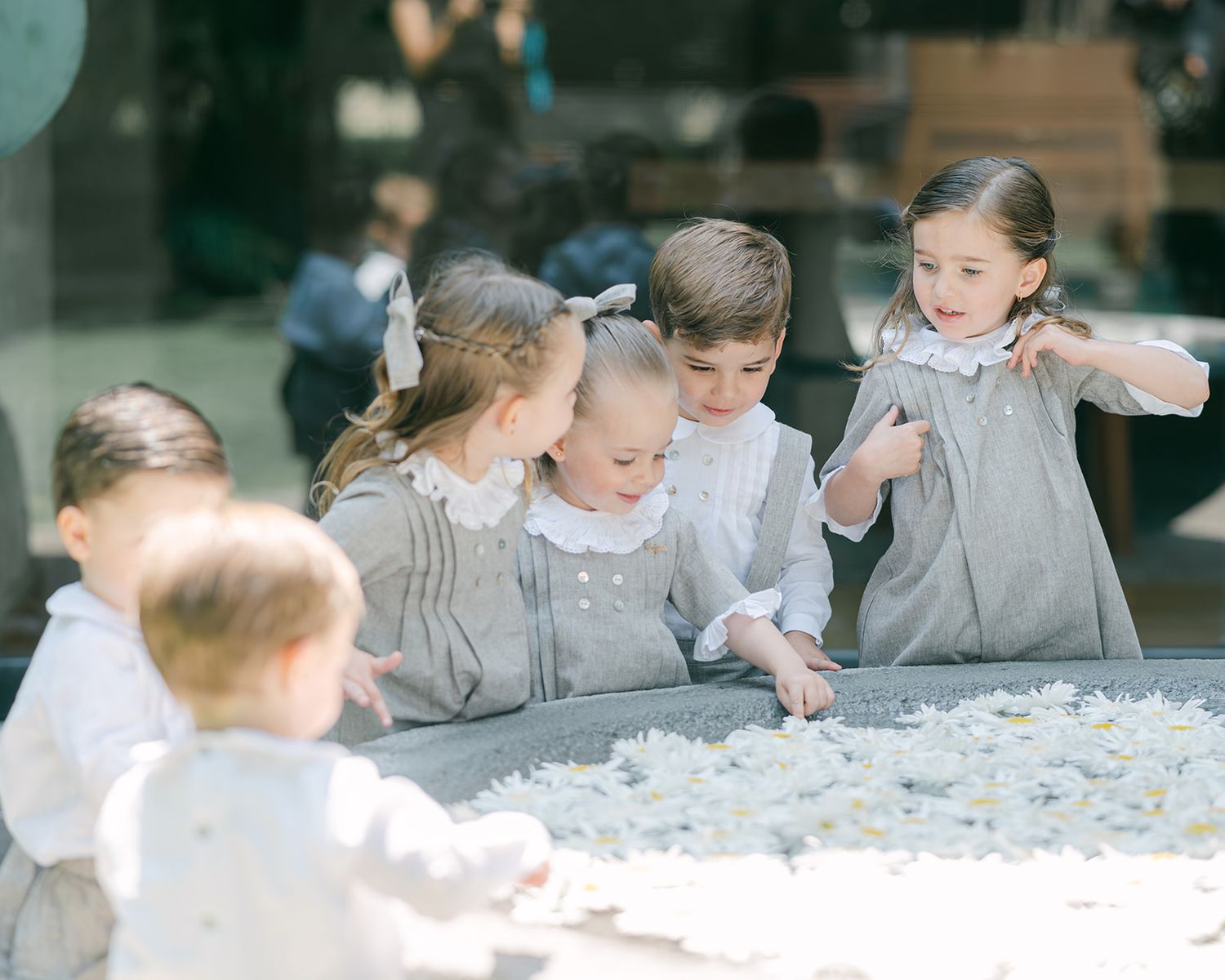 Group of young children in matching gray outfits gathered around white flower petals at wedding.