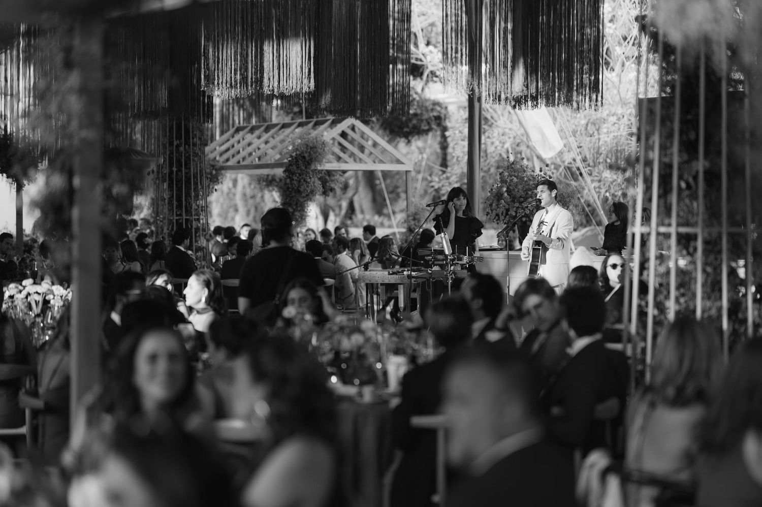 Black and white photo of wedding guests enjoying an evening reception under hanging decorations.