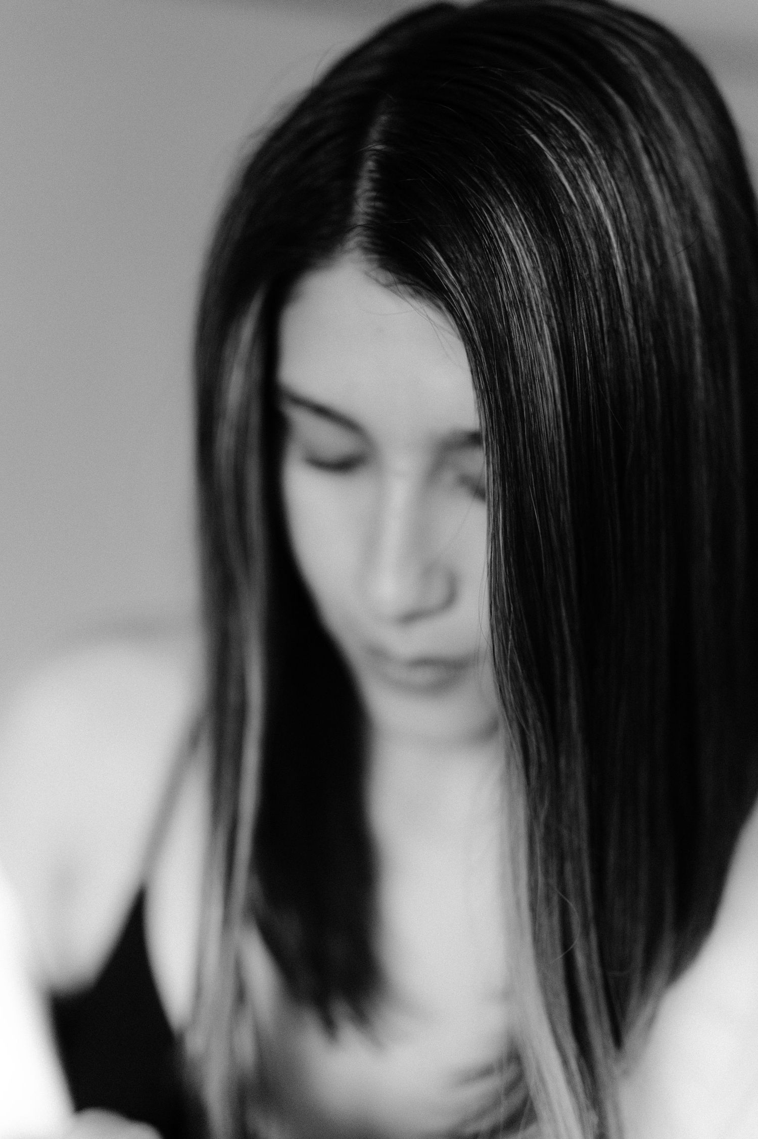 Black and white close-up portrait of woman with long dark hair looking down softly.