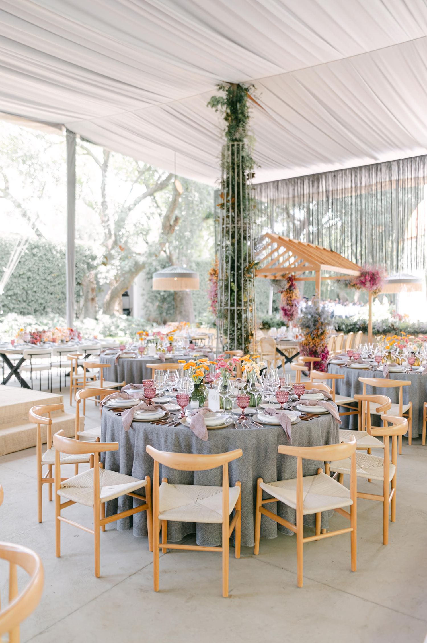 Elegant wedding reception under a white tent with gray linen tables, wood chairs, and floral decor.
