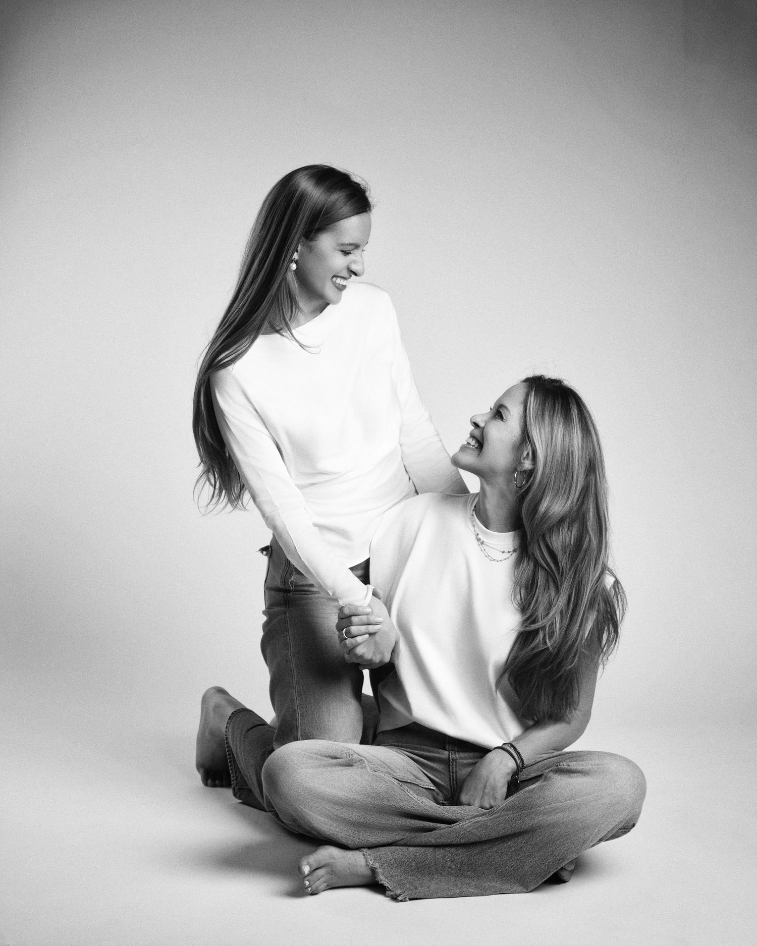 Two women laugh and hold hands in a joyful black and white studio portrait.