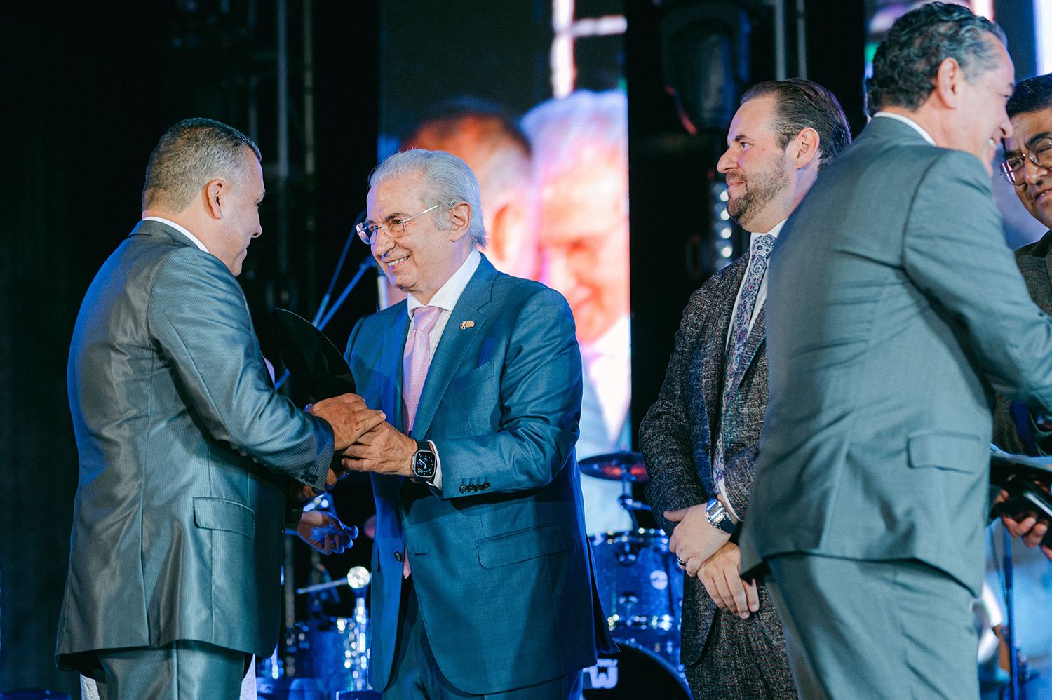 Business professionals in suits shaking hands on stage at a formal corporate event.