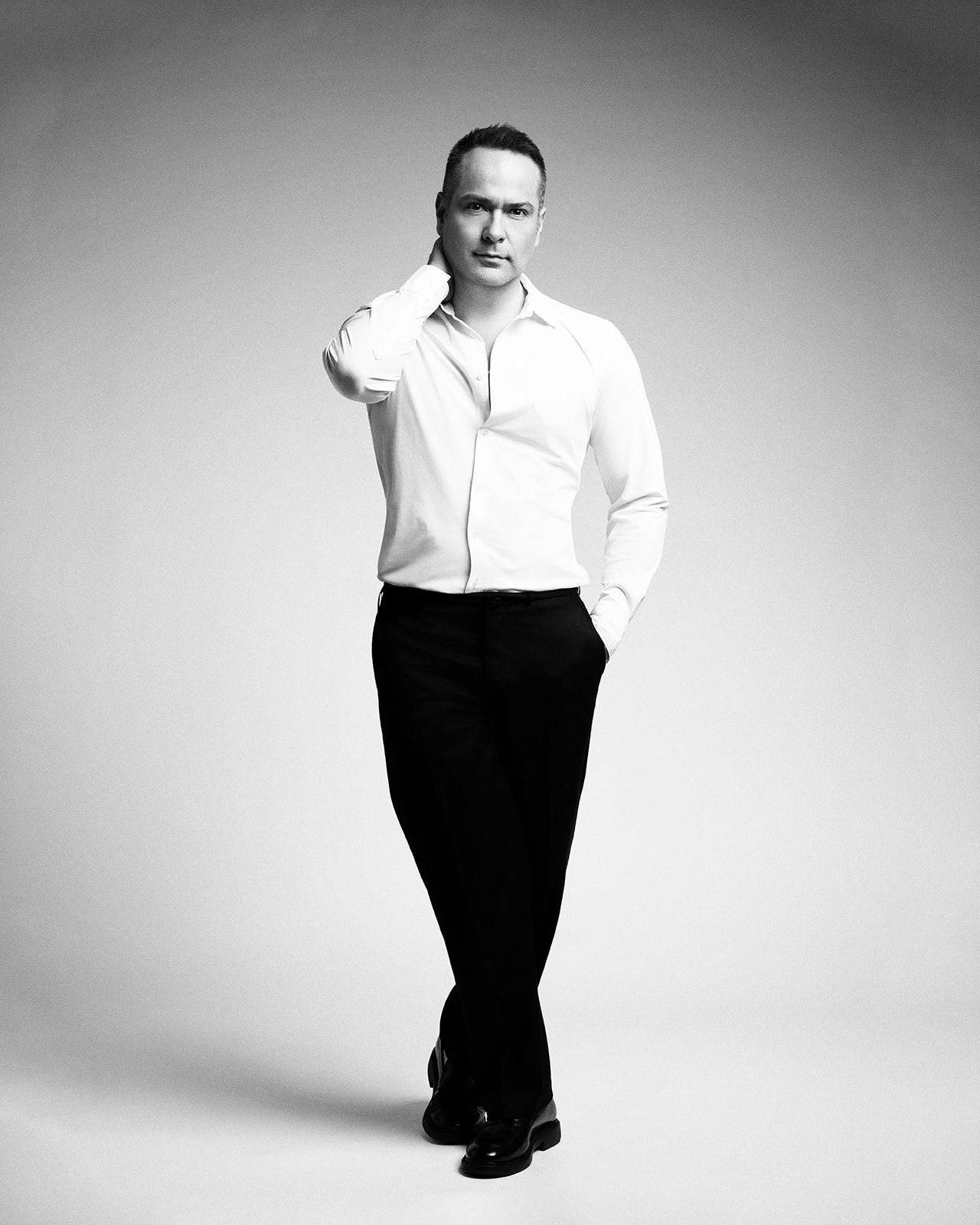 Black and white portrait of a man in white shirt and black trousers posing confidently in a studio.