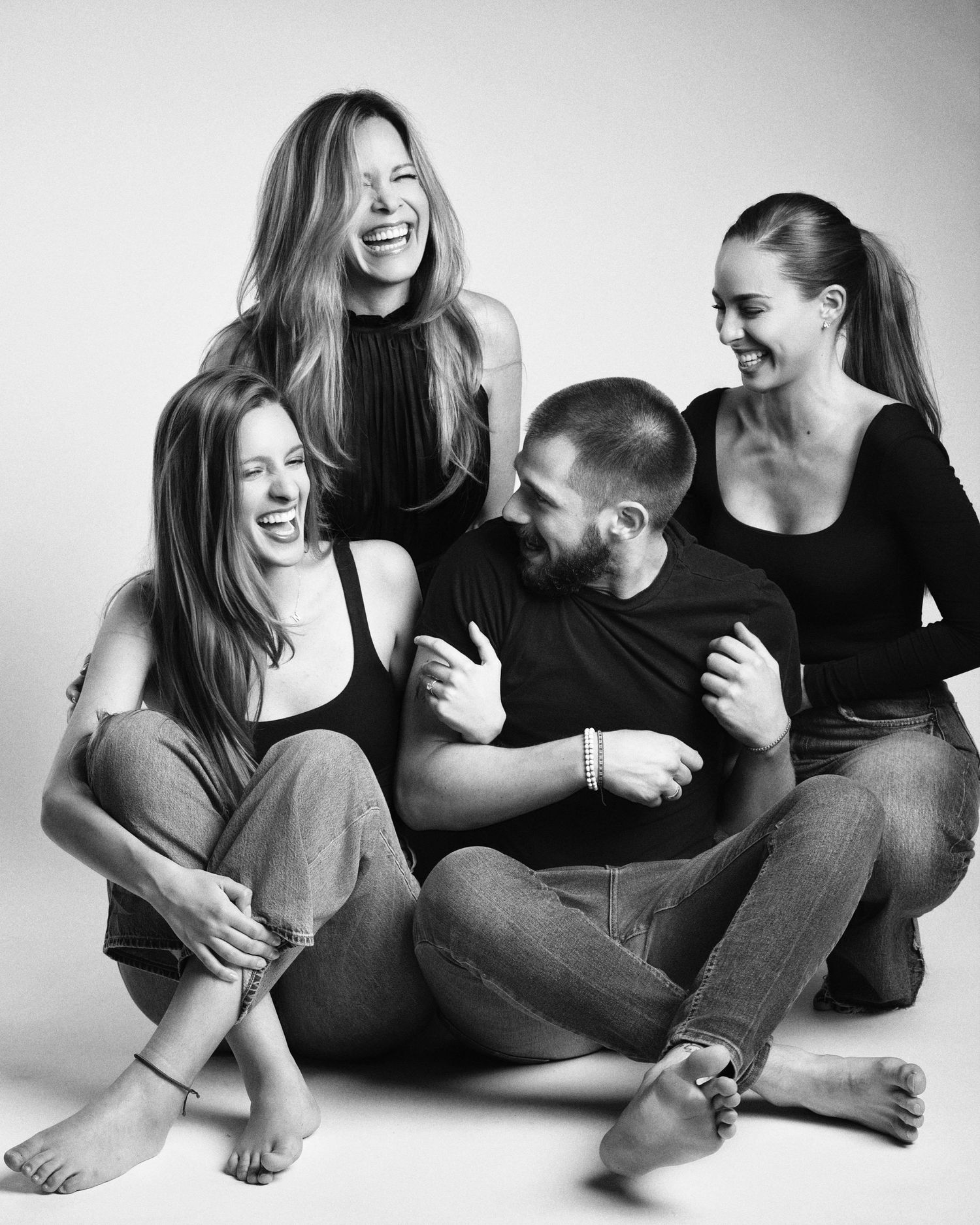 Black and white photo of four friends laughing and sitting together on the floor in casual outfits.