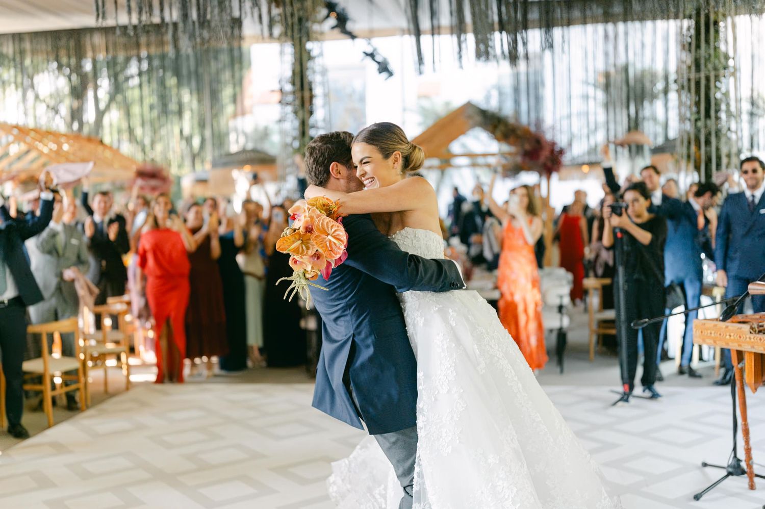 Wedding ceremony venue features dramatic lighting and hanging greenery with guests seated in rows.