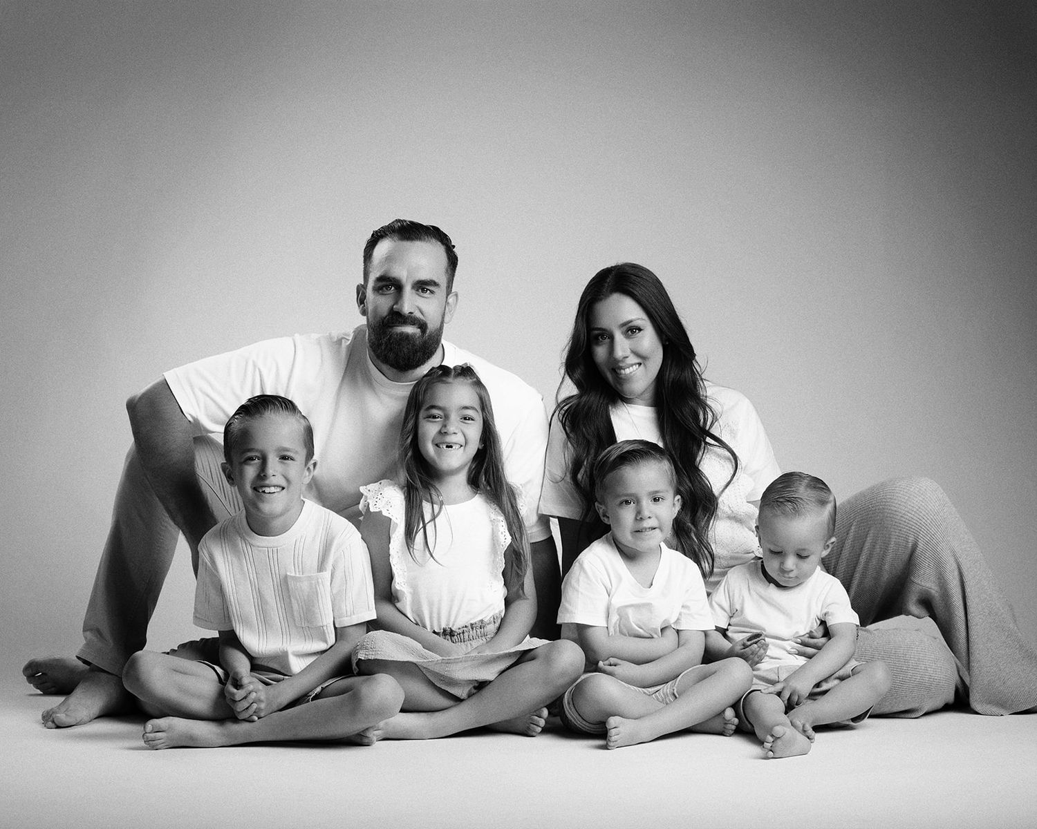 Black and white family portrait of parents with four young children sitting together in studio.