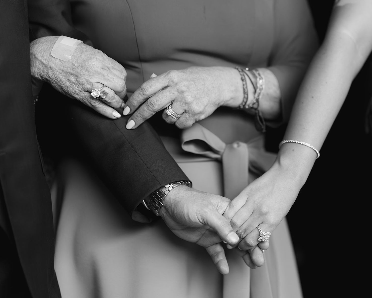 Black and white close-up of three people holding hands showing elegant rings and bracelets.