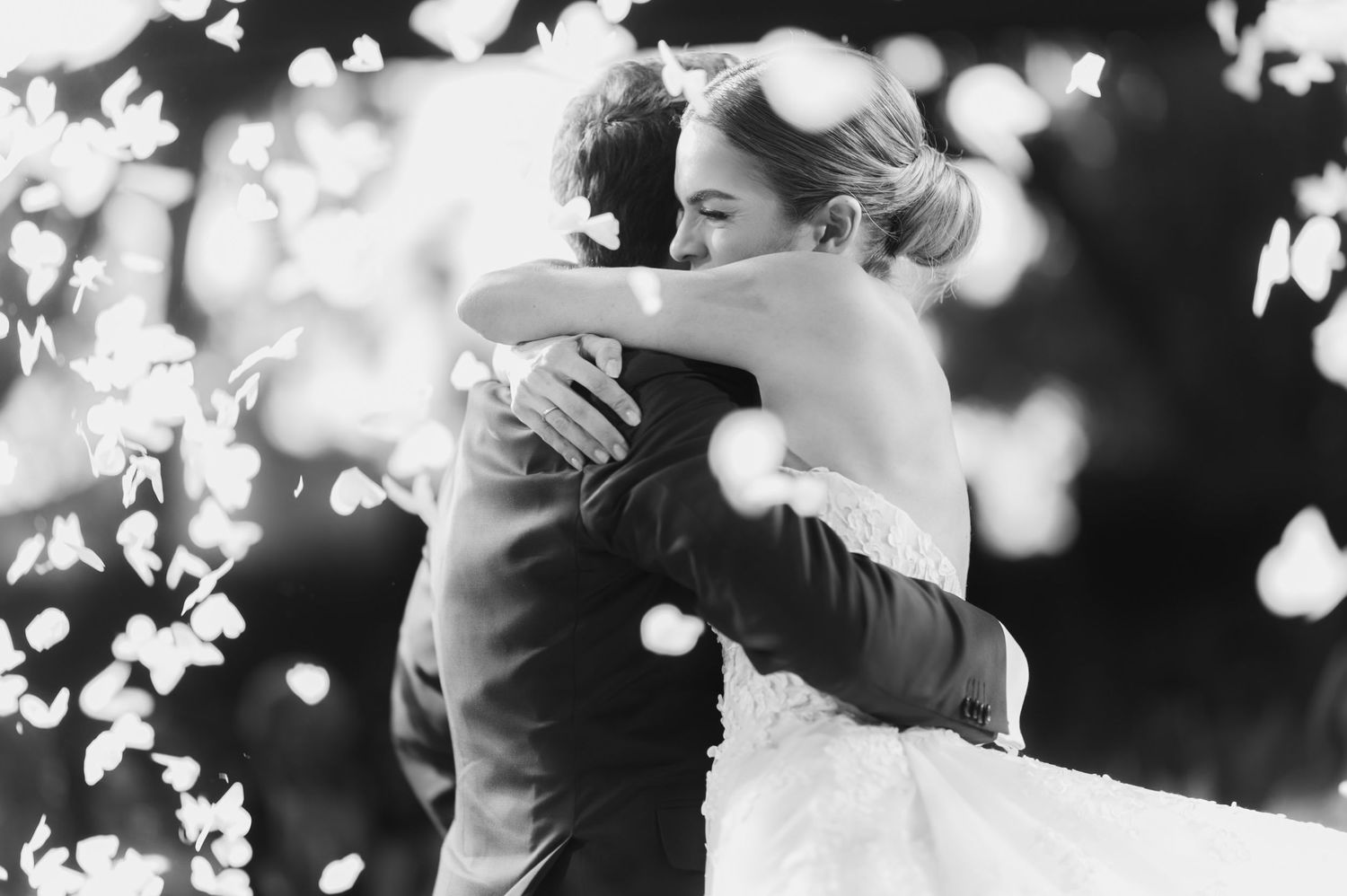 Black and white photo captures an intimate embrace during an outdoor wedding dance.