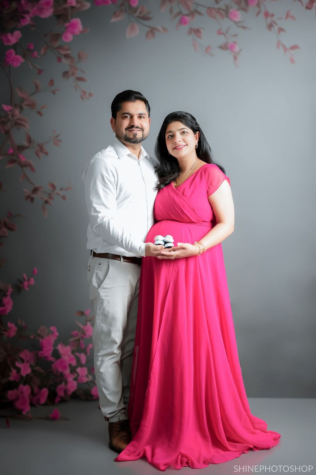 Maternity studio shoot with pink floral decor and coordinated outfits.