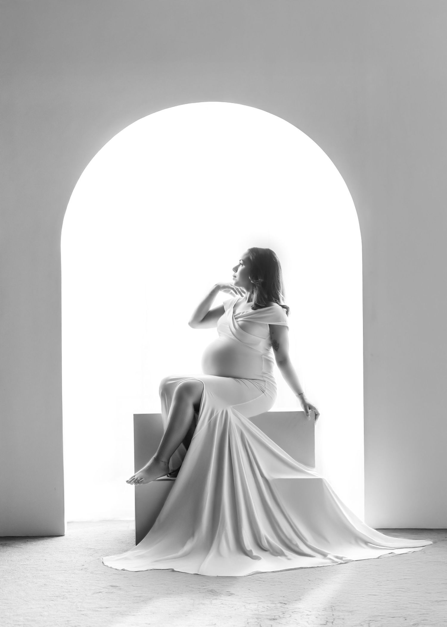 Minimalist maternity silhouettes in white against arched windows creating dramatic lighting.