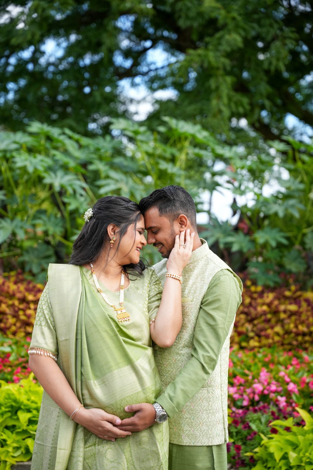 A couple wearing matching light green outfits shares tender moments in a flowering garden.