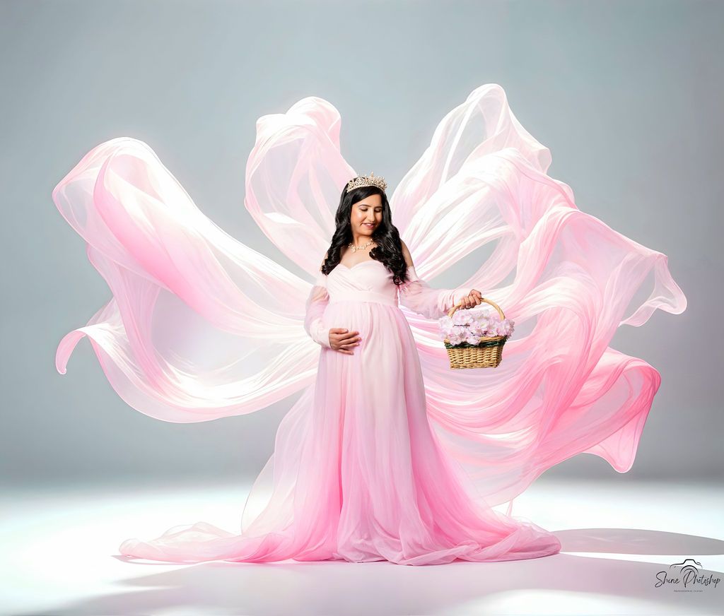 Flowing pink fabric creates ethereal effect in elegant maternity studio portrait.