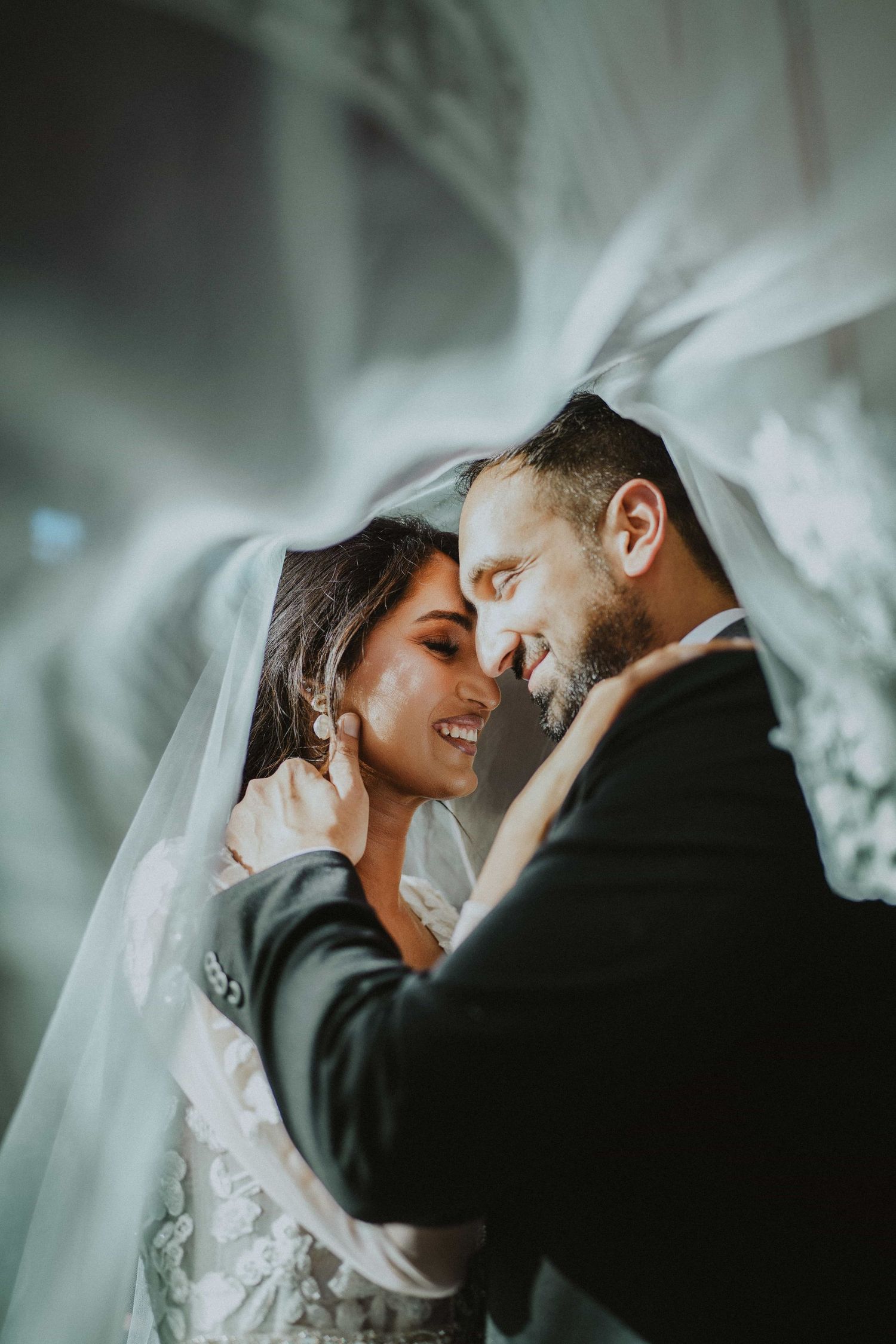 Intimate black and white wedding portraits showing tender moments between newlyweds under a flowing veil.