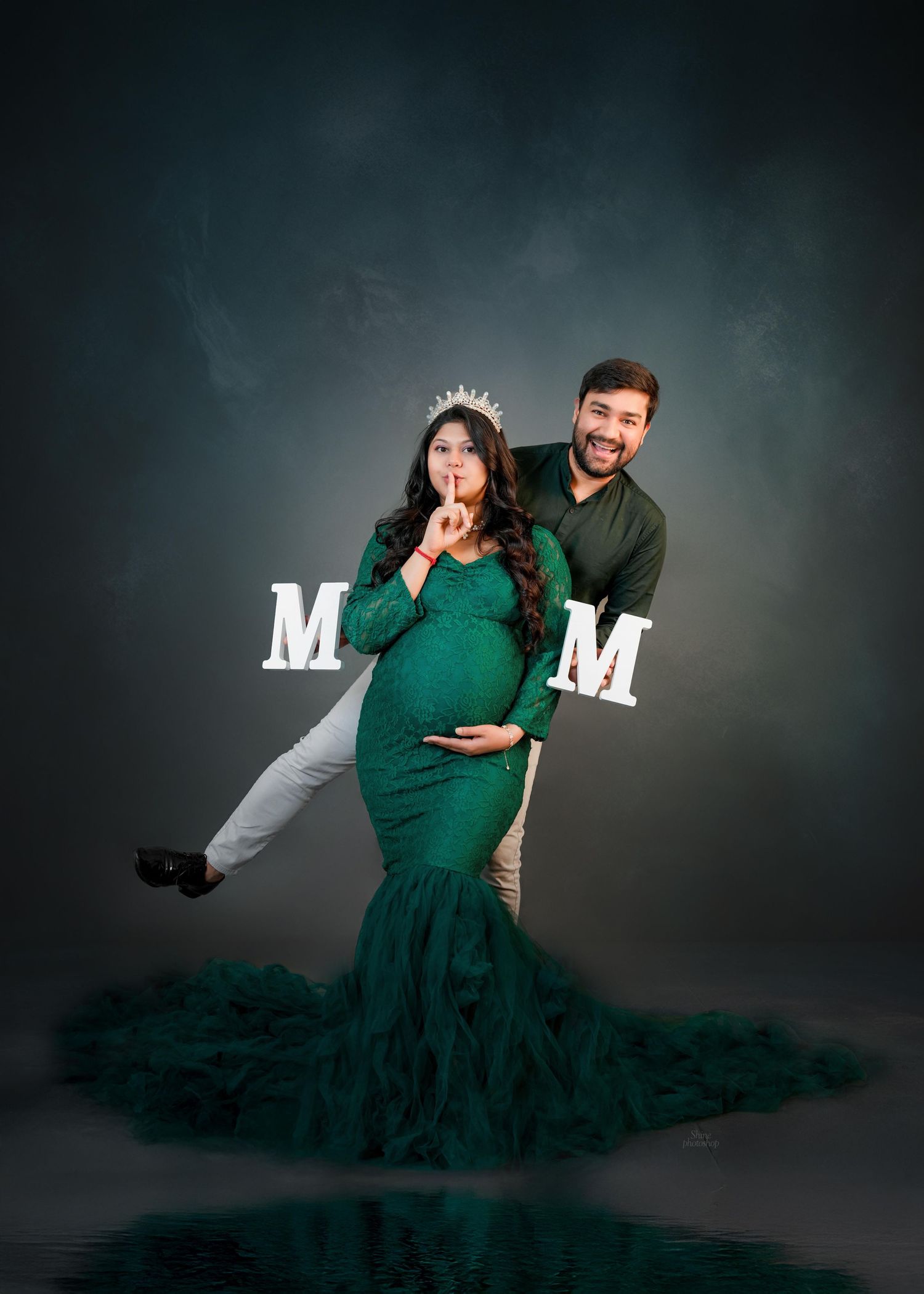 Creative maternity photoshoot with decorative letters and emerald dress against dark backdrop.