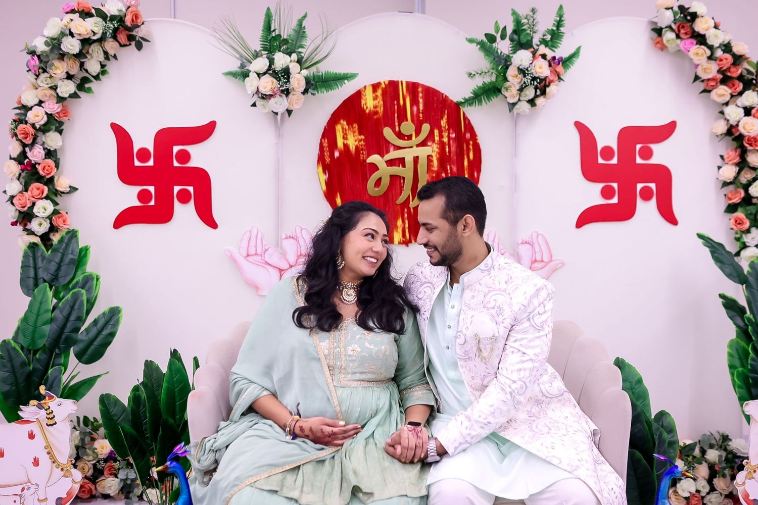Expectant couple shares joyful moments during baby shower photoshoot with traditional Hindu decorations.
