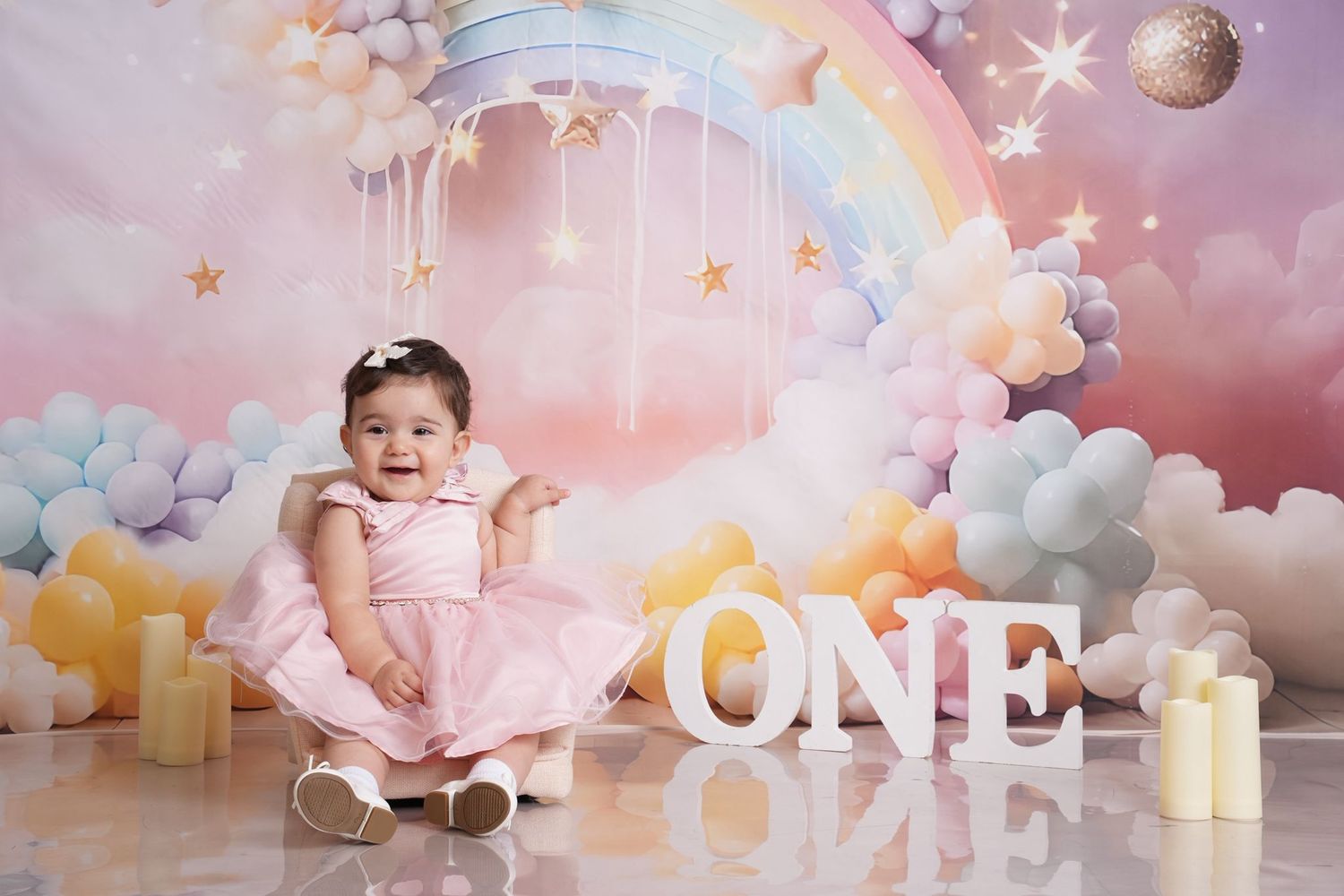 First birthday celebration setup with pink cake and dreamy pastel rainbow backdrop.