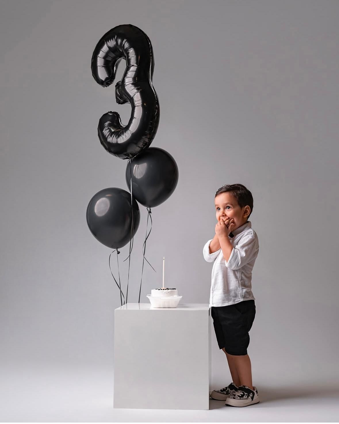 Birthday photoshoot with black number balloons and cake against white backdrop.