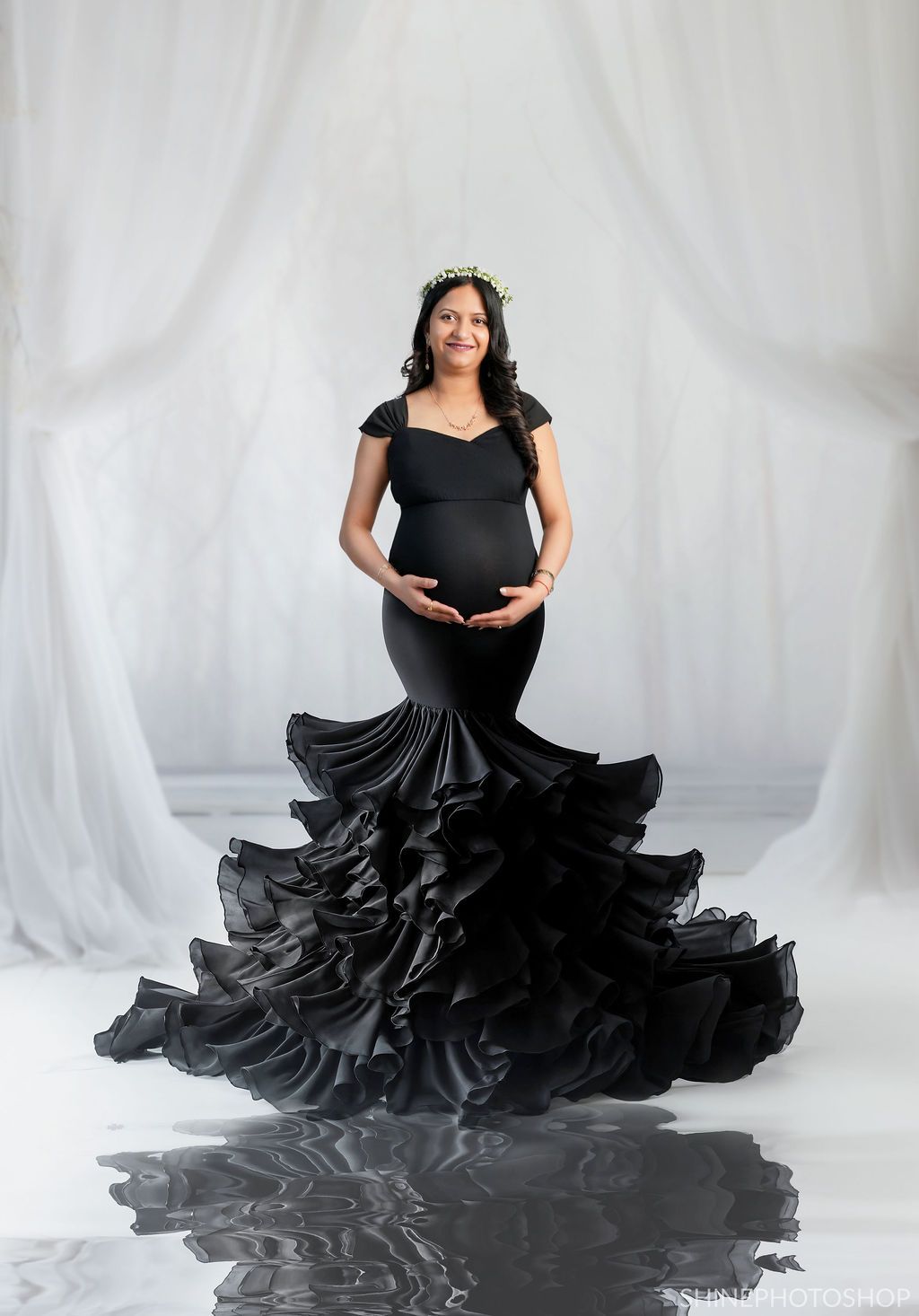 Maternity photoshoot featuring flowing black gown with dramatic ruffles against white backdrop.