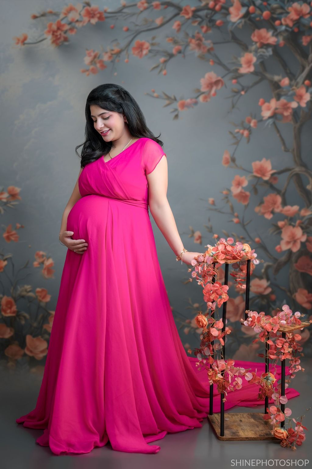 Maternity photos with pink cherry blossom decor and flowing fuchsia gown.
