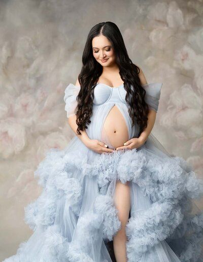 Dreamy maternity portraits in a flowing powder blue tulle gown against neutral backdrop.