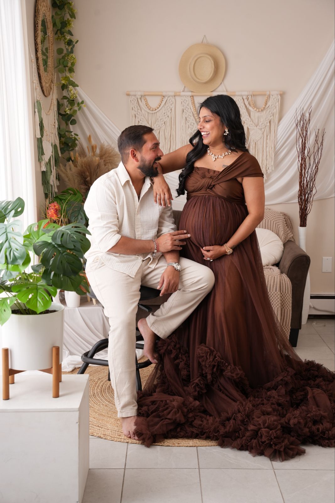 Couple sharing a tender moment during a boho-styled maternity photoshoot, woman in brown tulle gown cradling her baby bump.