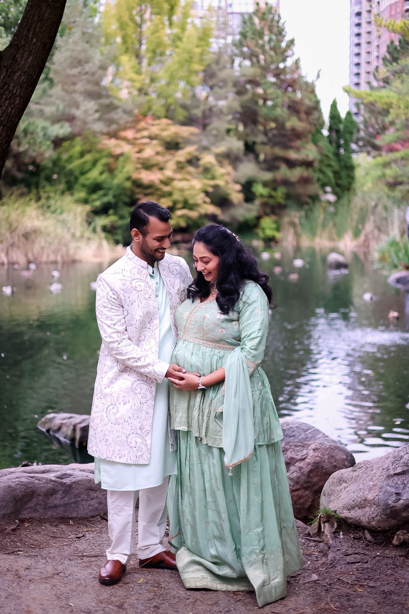 A couple in coordinated white and mint green outfits share a tender moment by a pond.
