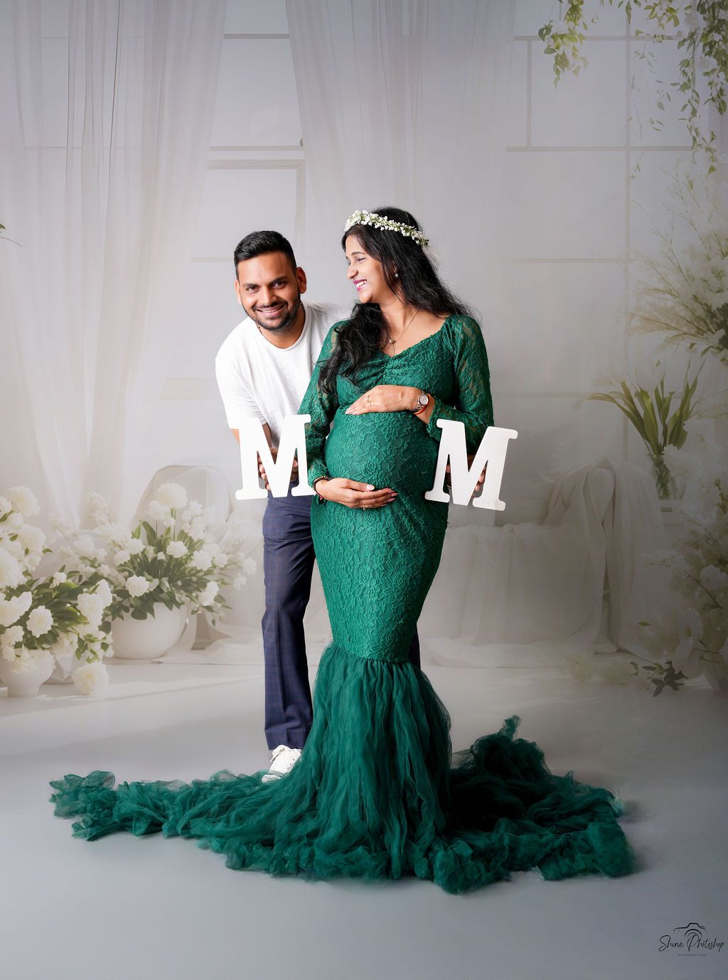 Maternity photo with decorative M&M letters and a flowing emerald green dress in a bright studio setting.