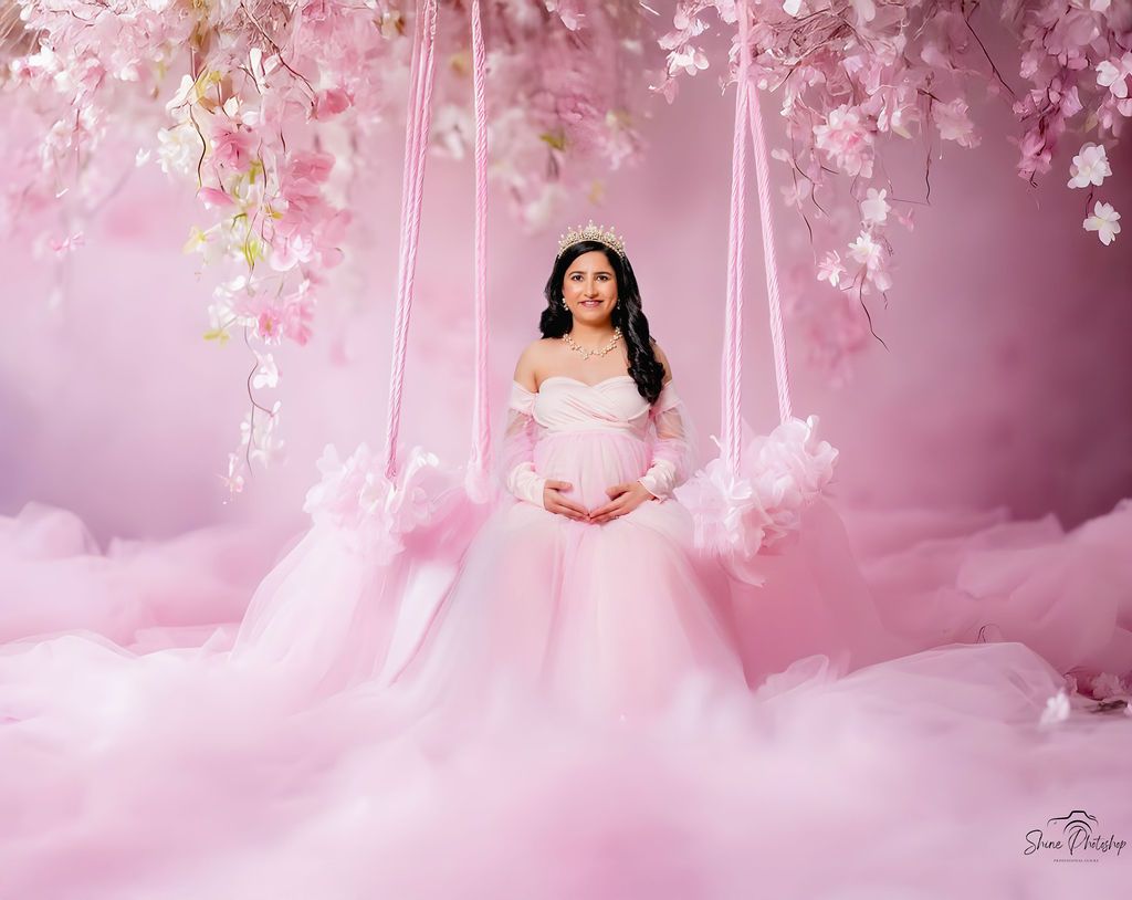 Dreamy maternity portrait with pink cherry blossoms and soft lighting effects.