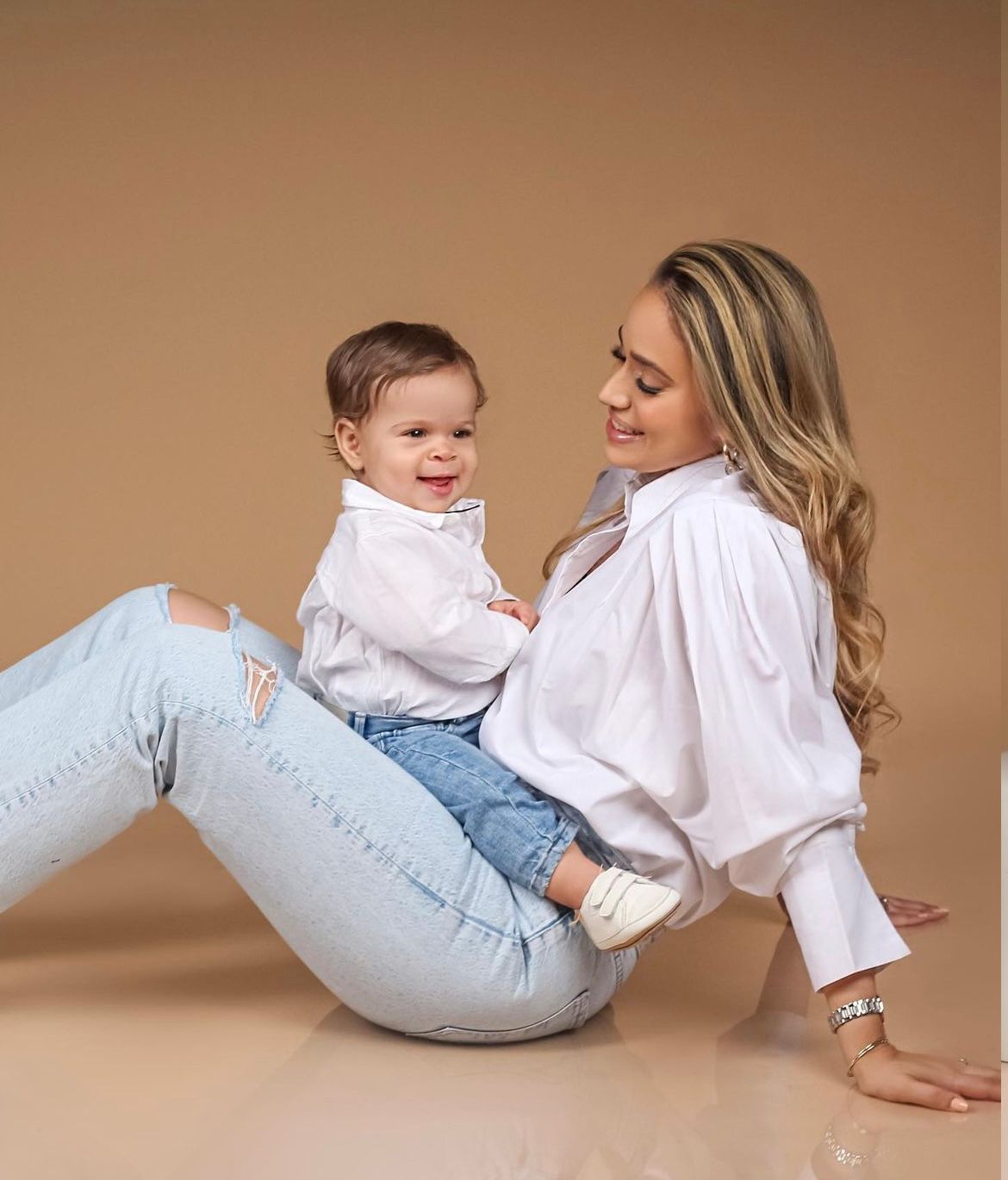 Mother and child in casual denim and white outfits playing on brown backdrop.