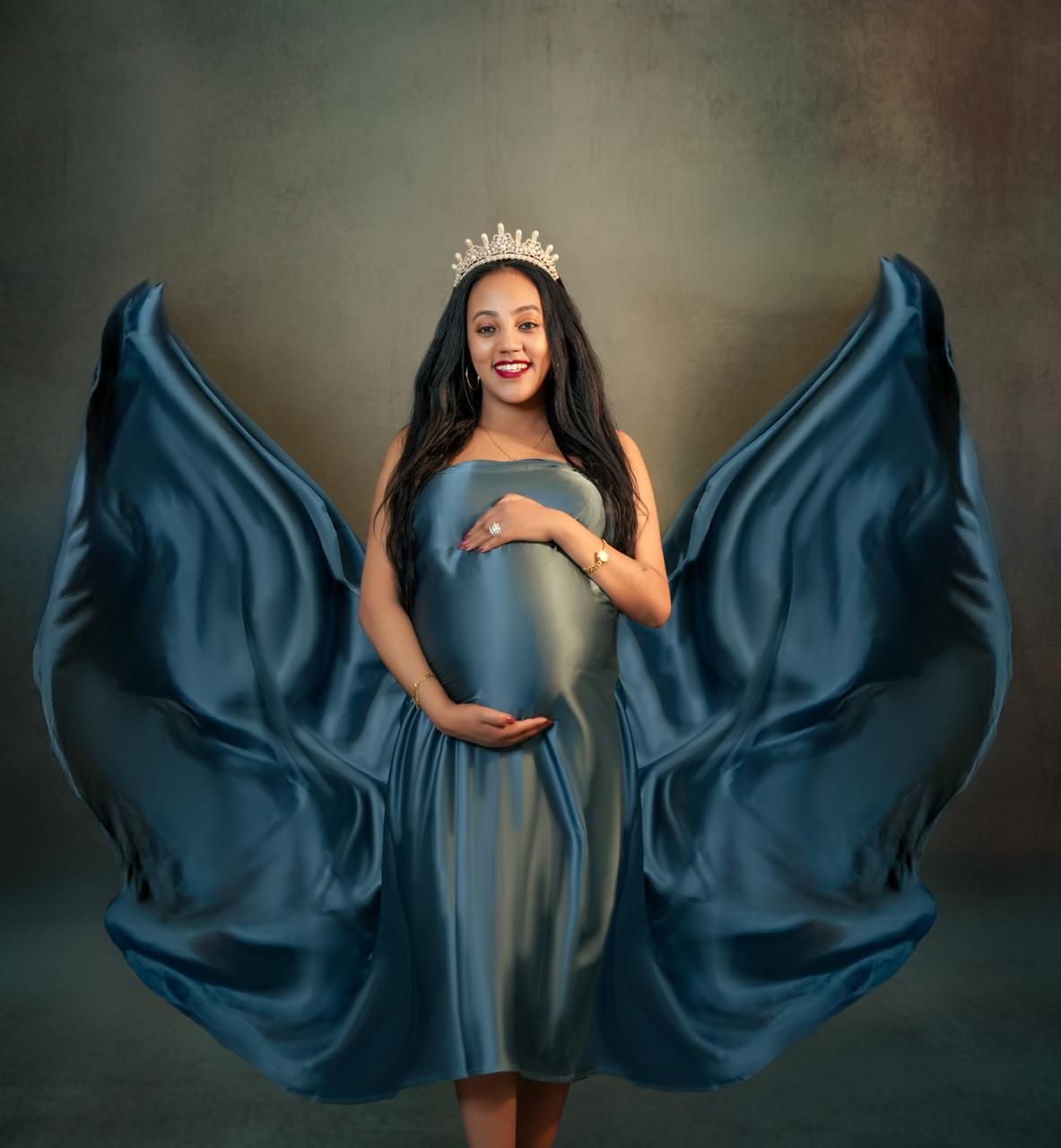 Maternity photo series showing flowing navy blue fabric dramatically billowing around a woman in a dark dress.