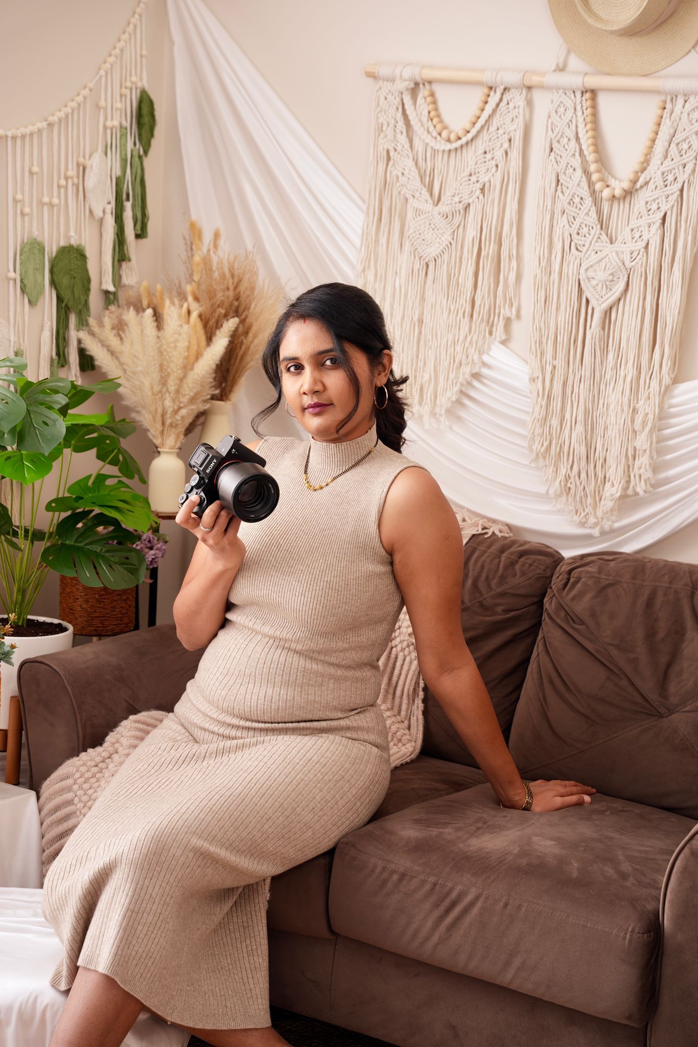 Four photos of someone in a cream knit dress posing on a brown couch with macrame wall decor and plants in the background.