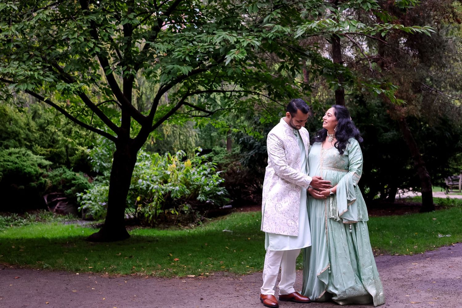 A couple in coordinated outfits walks through a lush green park setting.