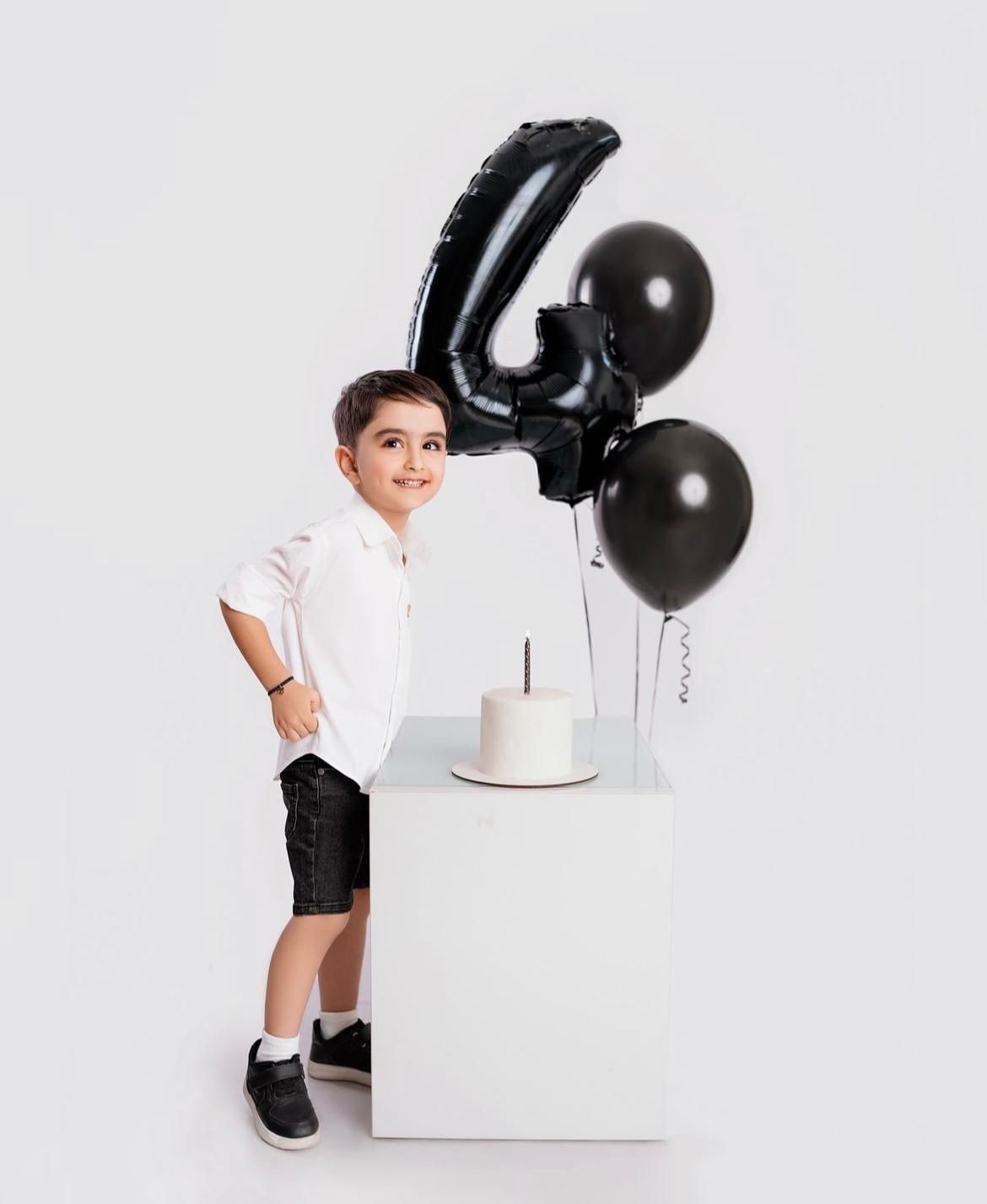 Minimalist birthday photoshoot setup with black balloons and white cube.