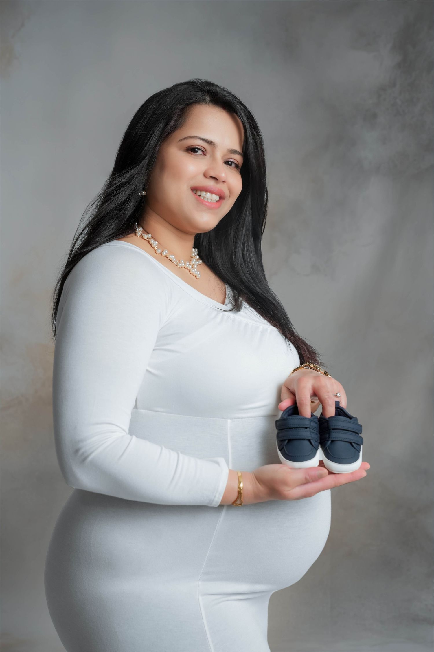 A series of artistic maternity portraits in white against a gray backdrop showing different poses.