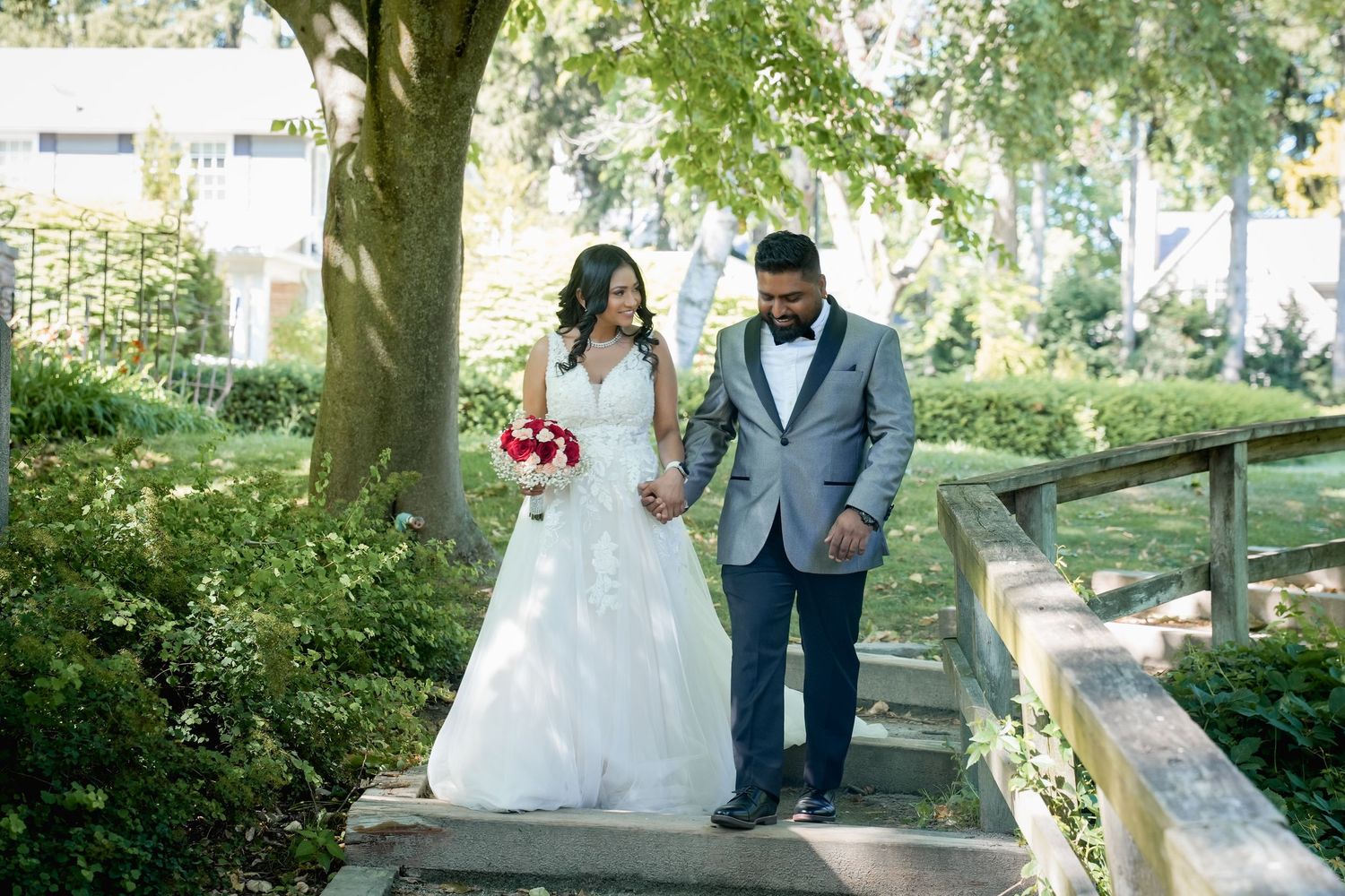 A couple in wedding attire walks together through a lush garden pathway on their special day.